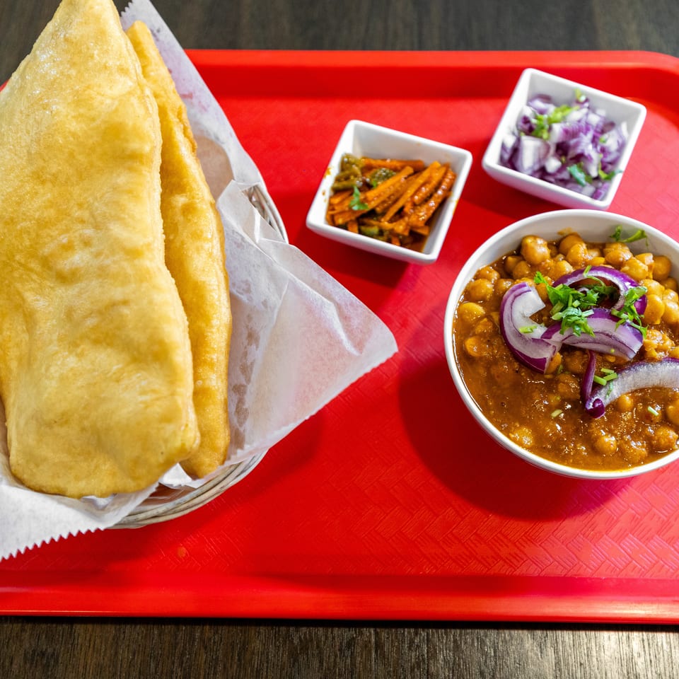 Indian meal on a red tray with fried breads, chickpea curry, spiced carrots, green chili pickle, and onion salad.