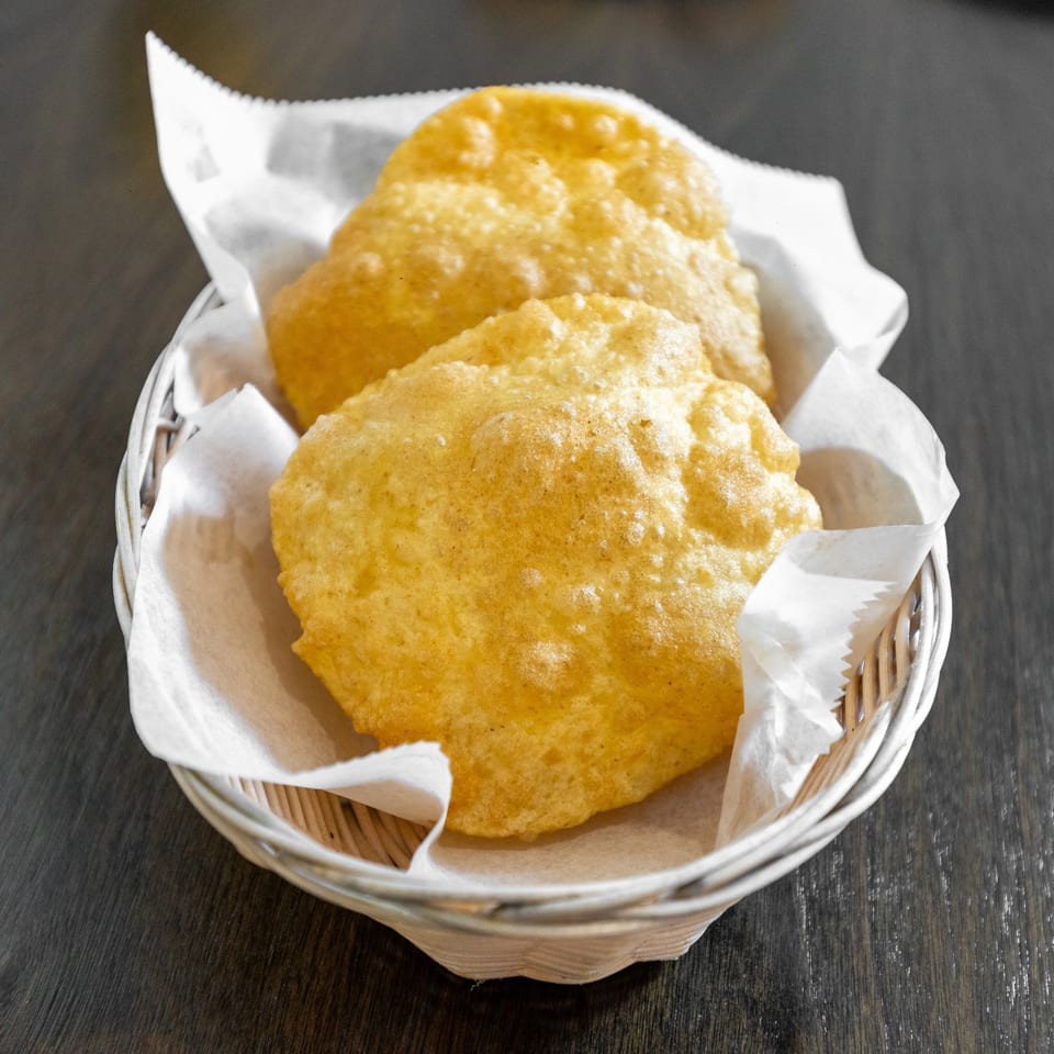 Basket of golden, puffed fried breads lined with white paper on a dark wooden restaurant table.