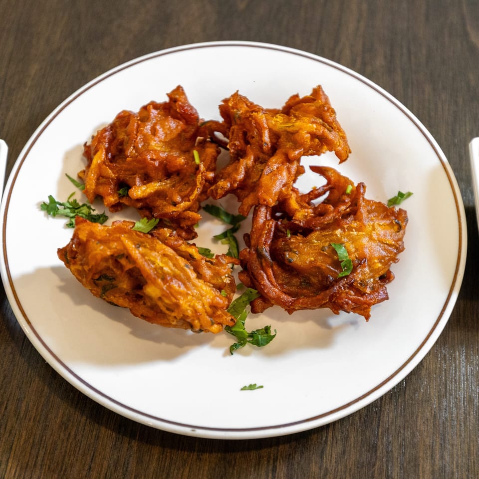 Crispy golden fritters garnished with cilantro on a white plate, served with green and brown dipping sauces.