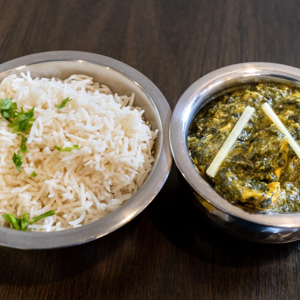 Metal bowls of white basmati rice garnished with cilantro and creamy spinach curry topped with ginger strips.