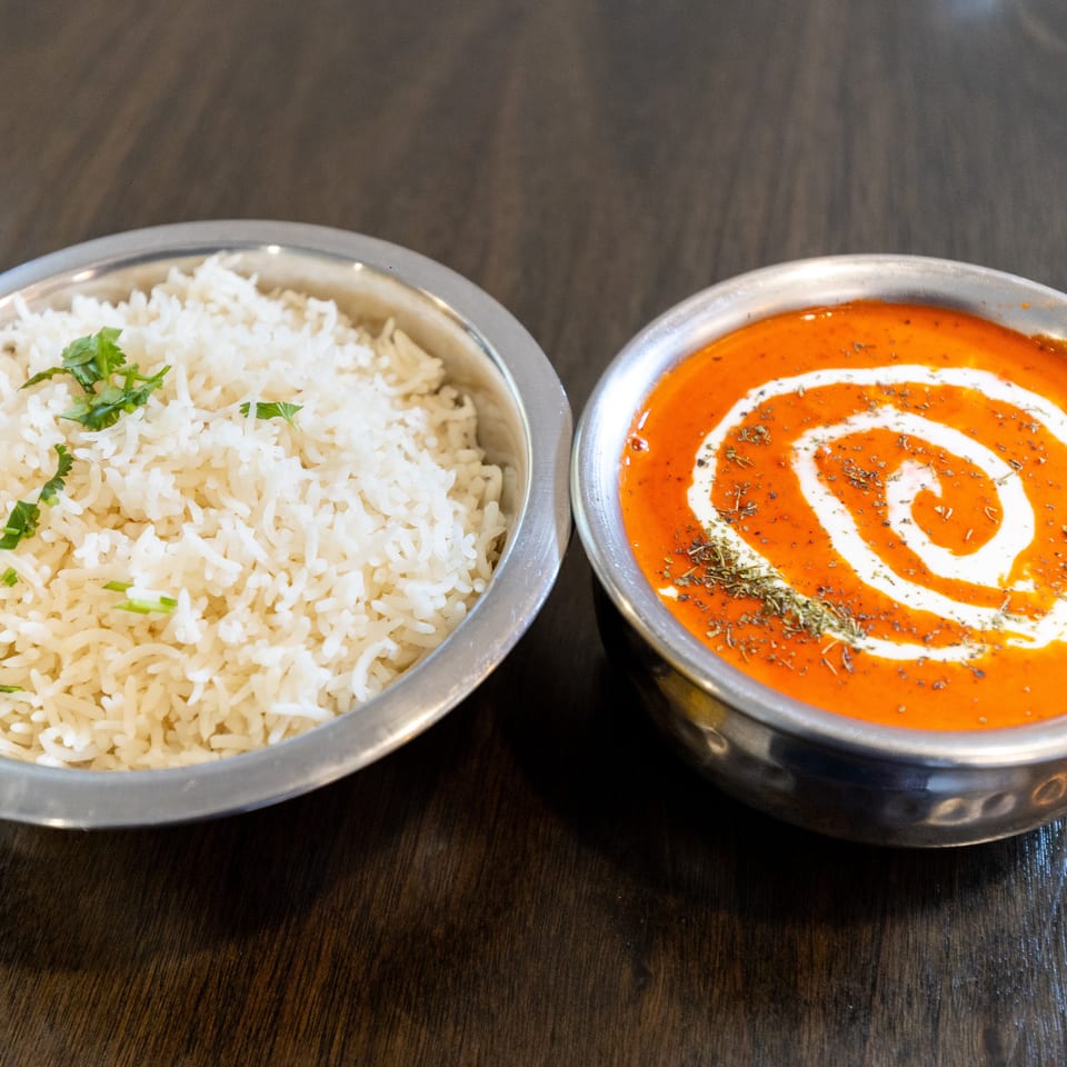 Bowls of steamed white rice garnished with cilantro and creamy orange curry topped with herbs on a wooden table.