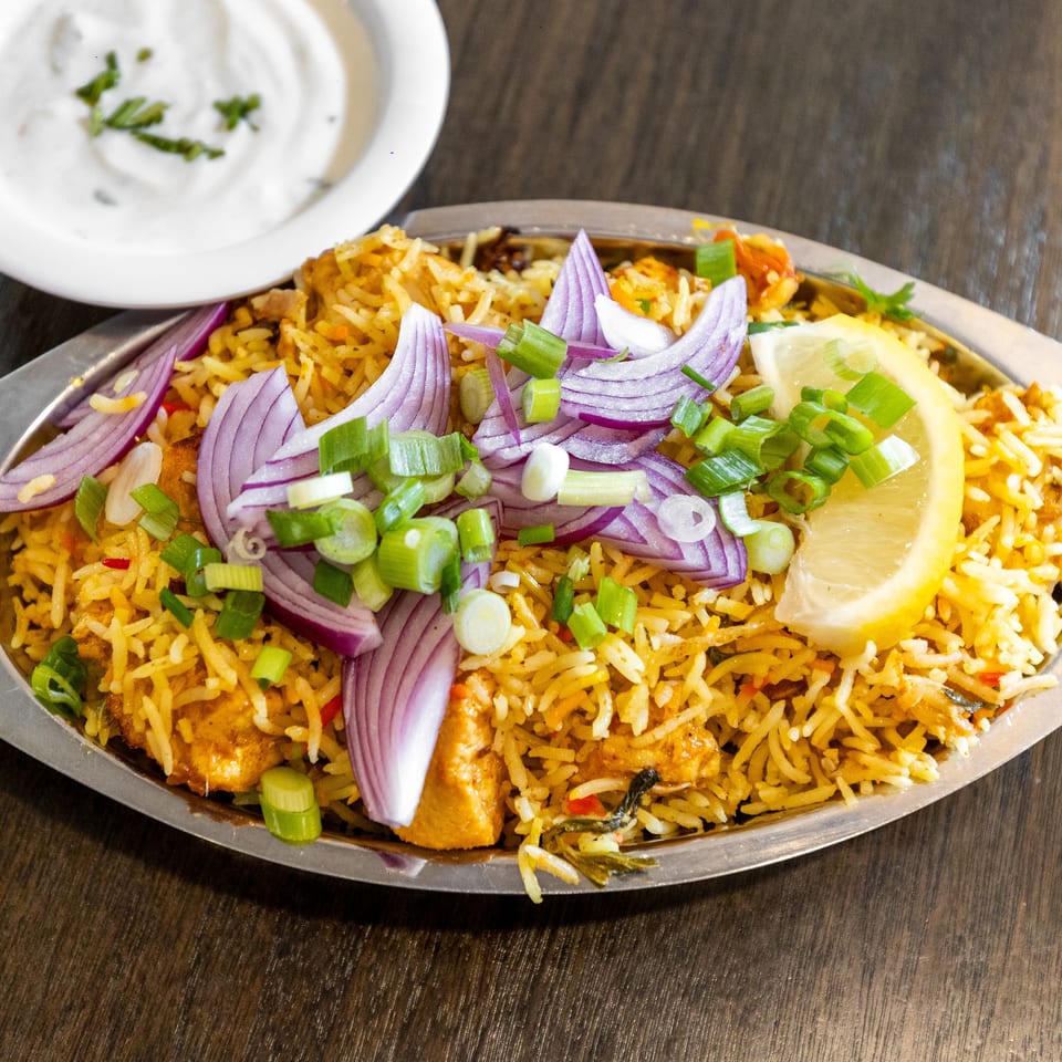 Spiced rice platter topped with chicken, red onion, green onions, lemon, and herbs on a metal serving tray.