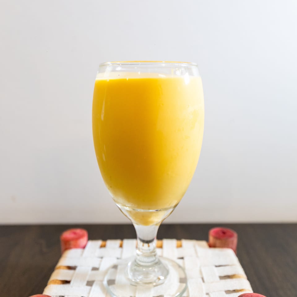 A stemmed glass filled with bright orange juice sits on a woven placemat atop a dark table.