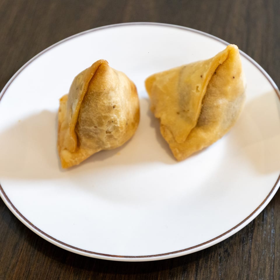 Two golden fried samosas served on a white plate with green and brown dipping sauces.