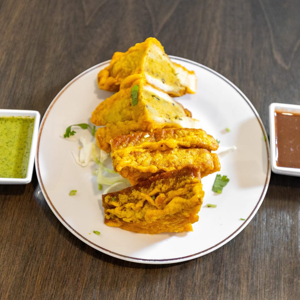 Golden fried appetizers arranged on a plate with green chutney and brown dipping sauce.
