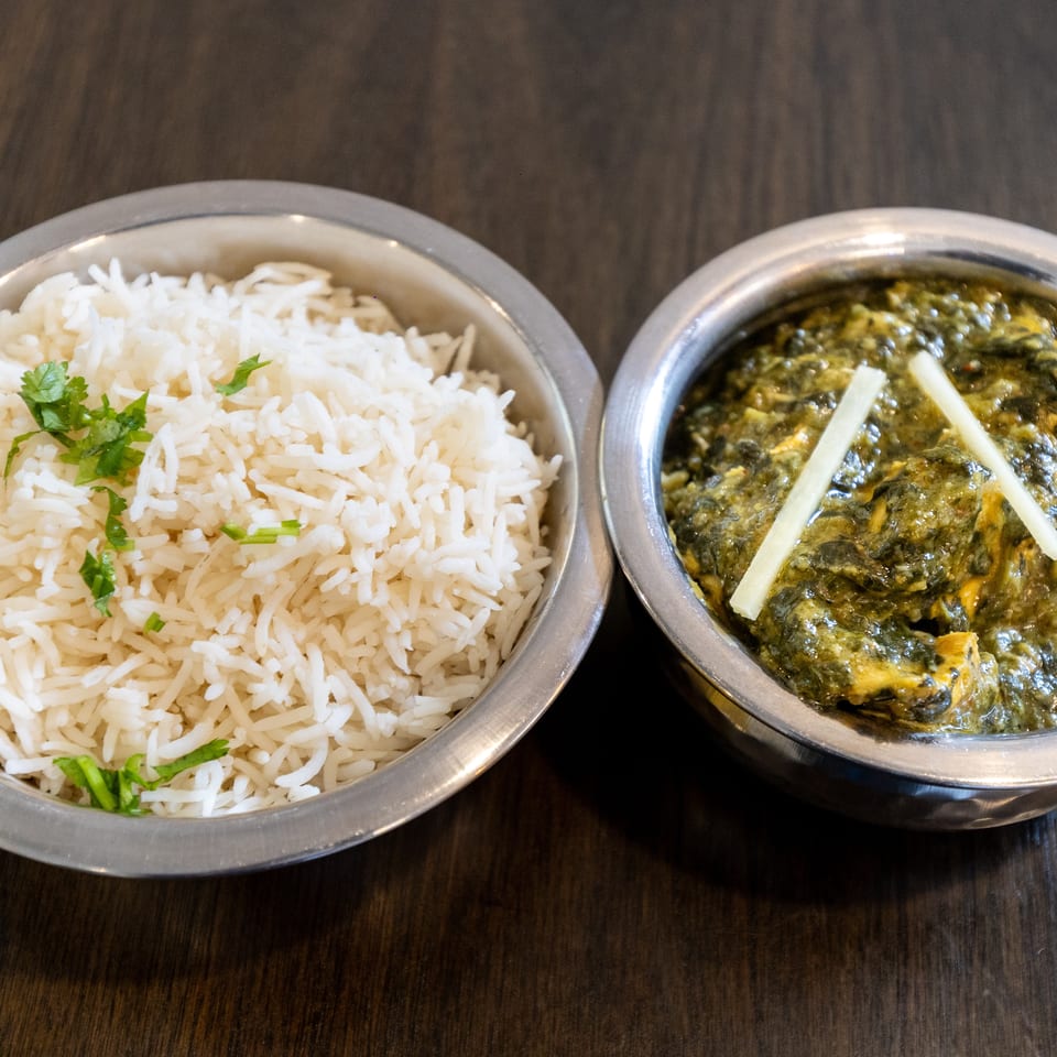 Metal bowls of white rice garnished with herbs and creamy green curry topped with ginger strips on a wooden table.