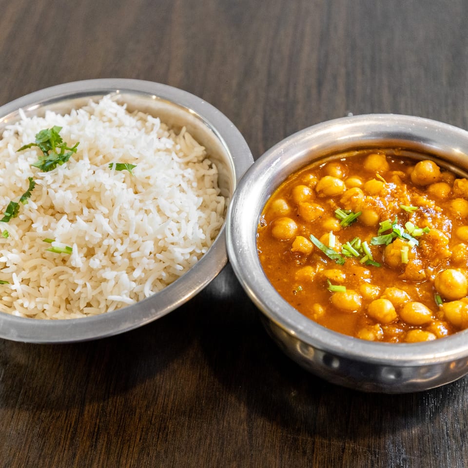Bowls of steamed white rice and chickpea curry garnished with fresh herbs on a dark wooden table.